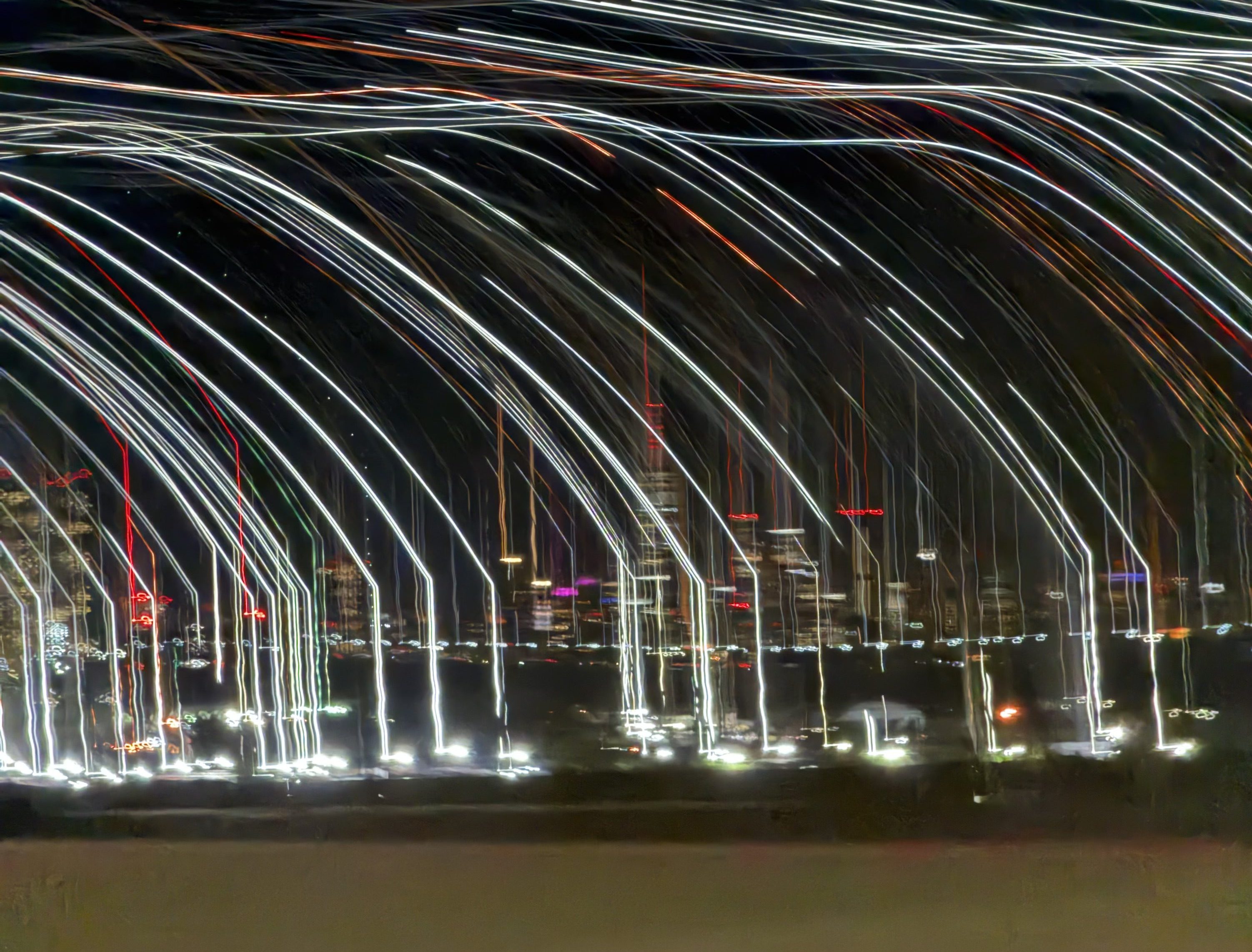 Abstract long-exposure photograph of the New York City skyline at night with white light trails and motion blur creating a cascading effect over illuminated skyscrapers.